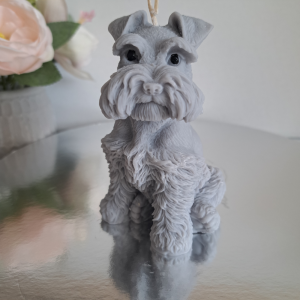 Ręcznie robiona naturalna świeca sojowa w kształcie szarego psa sznaucera, ustawiona na lustrzanej podstawce, z kwiatami w tle - AtmosHome.pl