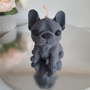 Recznie robiona naturalna swieca sojowa w ksztalcie ciemnoszarego psa buldoga francuskiego, ustawiona na lustrzanej podstawce, z delikatnie widocznymi kwiatami w tle - AtmosHome.pl