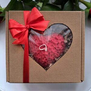 Czerwona świeca sojowa zapachowa w kształcie serca o strukturze drobnych kwiatuszków w eleganckim brązowym pudełku z okienkiem i czerwoną kokardą.