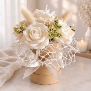 Elegancki flower box w stylu boho ze świecami sojowymi w kształcie białych róż, stabilizowaną gipsówką, trawami i koronkową siatką – Atmos Home.